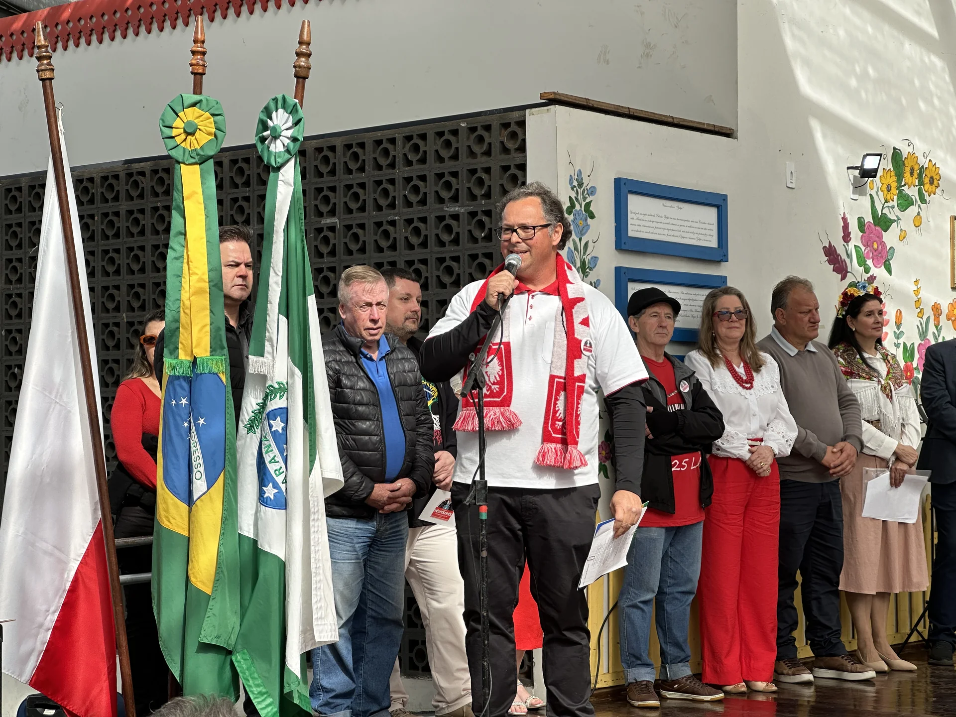 Representante cultural discursa diante das bandeiras do Brasil, Paraná e Polônia.